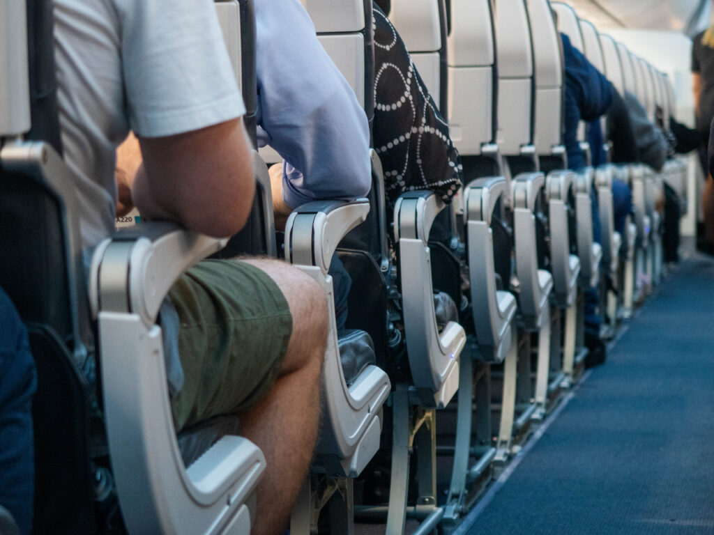 Photograph of three passengers on the left side of the airplane using the armrests of their isle seat. 