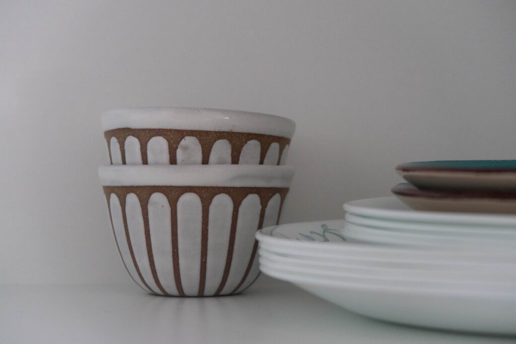 Image of two chai cups, Made by josephone mae design, in a cupboard next to a stack of plates.