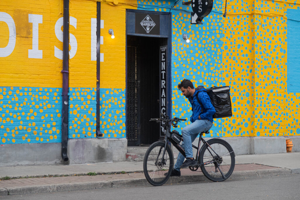 Delivery driver on an electric bike in front of bright yellow and blue wall.