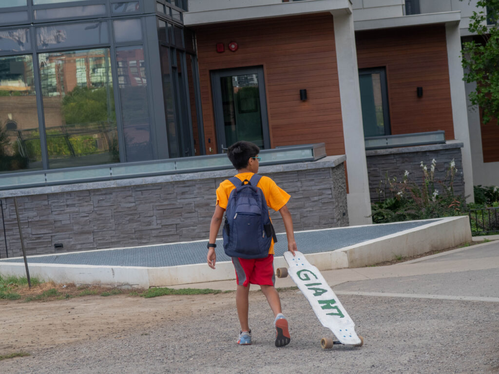 Young boy wearing a backpack and holding a hand painted longboard saying "giant"