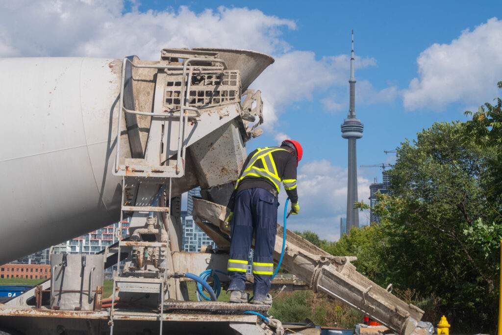 Construction worker cleaning cement truck in front of skyline depicting the Toronto CN Tower.